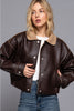 Woman wearing a brown leather jacket with beige interior on a gray background