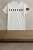 White t-shirt with 'FREEDOM' text and American flag graphic on a wooden surface.